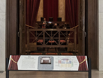 A volunteer docent delivers a Courtroom Lecture. Visitors may read information about 
                the Courtroom on an exhibit rail placed outside the Courtroom.