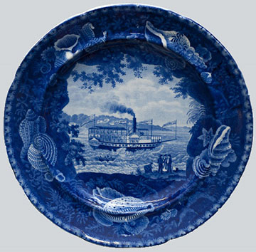 Chief Justice Marshall Steamboat plate by Enoch Wood & Sons, c. 1825 - 1846. The blue transfer plate features a shell border and depicts the steamboat traveling along the Hudson River. A launch holding several figures is tethered alongside the steamboat, likely having just ferried the group of passengers ashore.