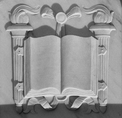In the uppermost area of the Great Hall are repeating architectural elements known as metopes, which depict classical symbols and famous lawgivers. The book flanked by torches shown here represents education and knowledge.