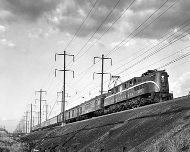 A Pennsylvania Railroad class GG1 locomotive, the same in Teller’s poster, here seen hauling a passenger train through Secaucus, New Jersey, on July 20, 1965. The engine’s shell had been designed by the prolific and influential industrial designer Raymond Loewy (1893–1986), who is closely associated with the streamlined Art Deco style of the 1930s.