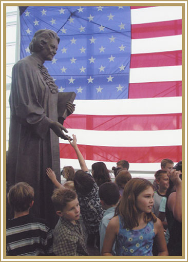 A bronze statue of Justice O’Connor on display at the Sandra Day O’Connor United States Courthouse in Phoenix, Arizona.  She is depicted wearing her judicial robe, carrying a volume of the U.S. Reports, and standing on shards of glass that represent the ceilings she shattered during her career.